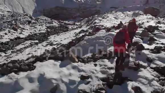 两位带着背包和照相机的女旅行者的空中景色穿过雪地和石头来到冰川之间视频的预览图