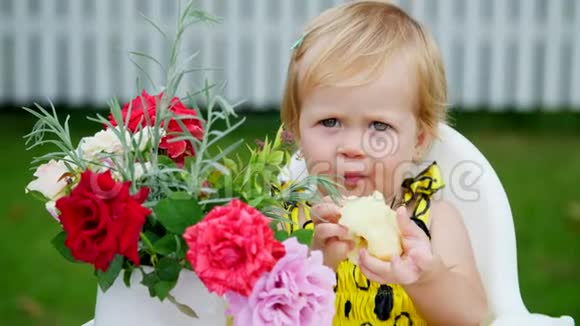 夏天在花园里肖像一岁漂亮的金发女孩吃一个苹果与猿猴在桌子上有一个视频的预览图