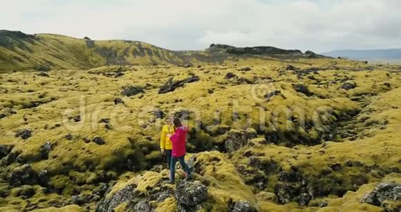 鸟瞰冰岛熔岩场上站在岩石上的游客妇女女性在大自然中使用智能手机视频的预览图