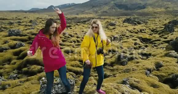 鸟瞰两个幸福的女人站在岩石上玩得开心跳舞冰岛的熔岩覆盖着苔藓视频的预览图