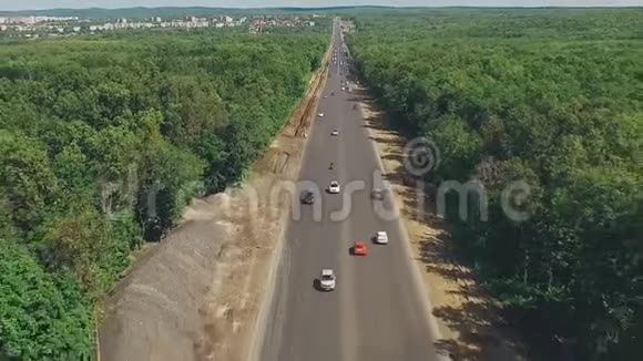 在阳光明媚的夏日里无人机在笔直的长公路上飞过茂密的森林视频的预览图