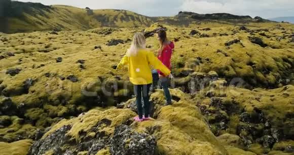 鸟瞰两个女人站在岩石上看着冰岛的熔岩场跳舞感受自由快乐视频的预览图