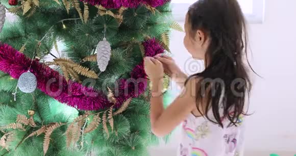 可爱的小女孩在圣诞树上挂装饰品视频的预览图