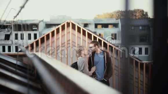 年轻的幸福夫妇站在屋顶上欣赏美丽的景色迷人的男人和女人在上面接吻视频的预览图