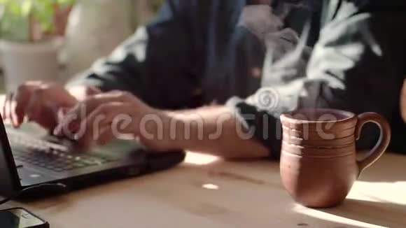 在咖啡馆里把茶杯和笔记本电脑放在桌子上杯子里满是棕色的热饮料它在挥手一个男人视频的预览图