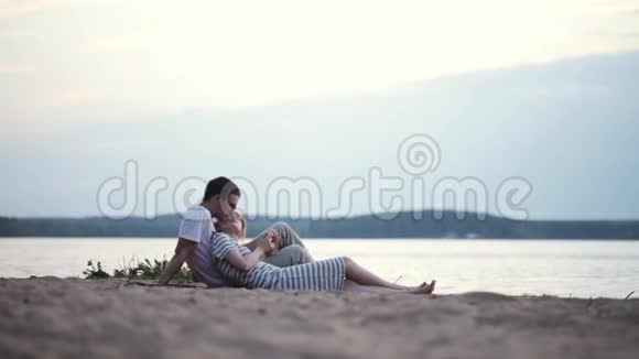 美丽的年轻夫妇坐在河边用智能手机男人和女人在海滩上休息视频的预览图