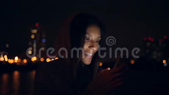美丽的年轻混血微笑的女人使用手机在夜城街道慢动作4K莫斯科俄罗斯视频的预览图