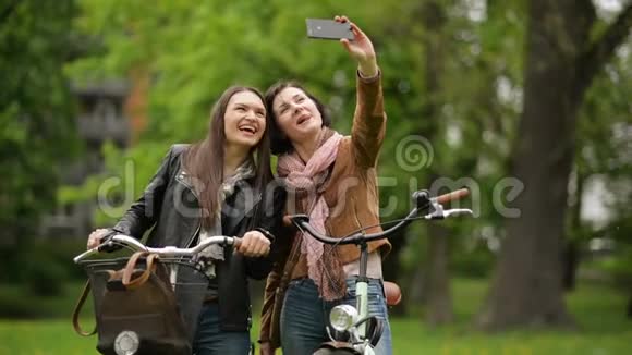 有趣的女朋友拿着自行车用智能手机自拍两个女孩正在拍照视频的预览图