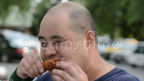 一个肥胖的亚洲秃头泰国男人贪婪地咬着吃炸鸡鸡腿饿得满脸都是冷汗视频的预览图