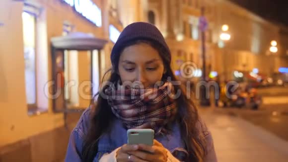 微笑的白种人女孩在手机上发短信走在夜晚的圣彼得堡的街道上4K慢动作俄罗斯视频的预览图