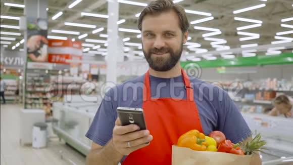 微笑超市员工使用手机拿着购物袋在超市视频的预览图