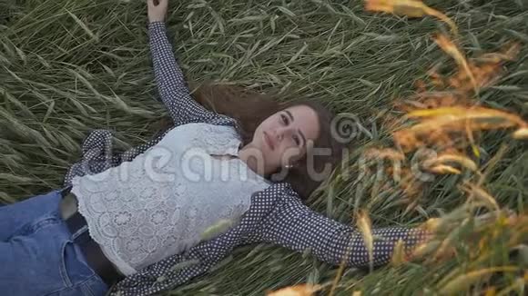 一个年轻漂亮的少女躺在柔和的夕阳下的麦田里视频的预览图
