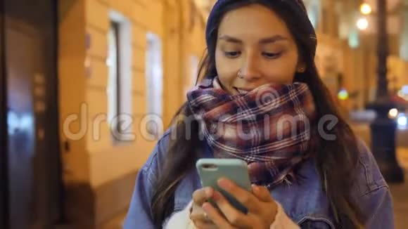 迷人的年轻混合种族微笑妇女使用手机在夜间步行圣彼得堡4k视频的预览图