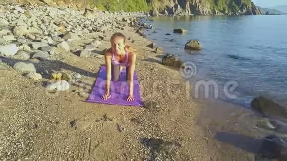 Flycam显示金发女郎手持瑜伽姿势对抗蔚蓝的海洋视频的预览图