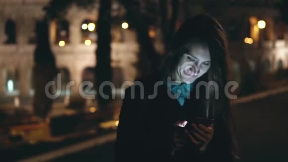 慢动作快乐的年轻女人在意大利罗马竞技场附近的公园里散步并使用智能手机视频的预览图
