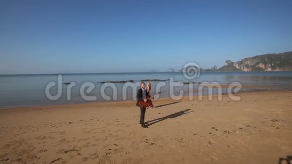 穿着红衣服的女孩在海滩上演奏黑色戏剧的胡子吉他手视频的预览图