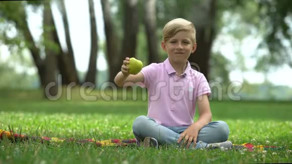 快乐的男孩坐在公园里拿着绿苹果健康的有机食品视频的预览图