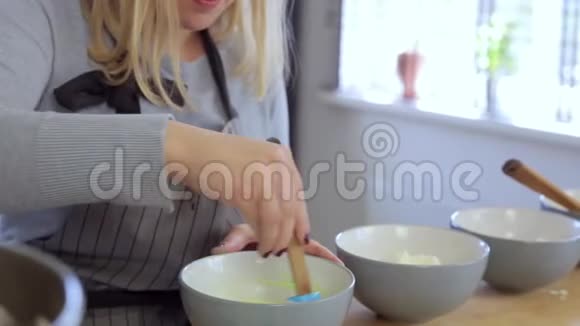 年轻漂亮的女人做甜点的彩色奶油把配料混合在碗里女性在厨房做饭视频的预览图