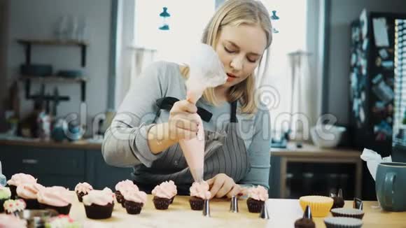 年轻漂亮的女人用糕点包里的奶油装饰小蛋糕金发糖果准备订单视频的预览图