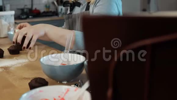 年轻的金发女人在厨房做纸杯蛋糕漂亮的女人用切割机做松饼视频的预览图