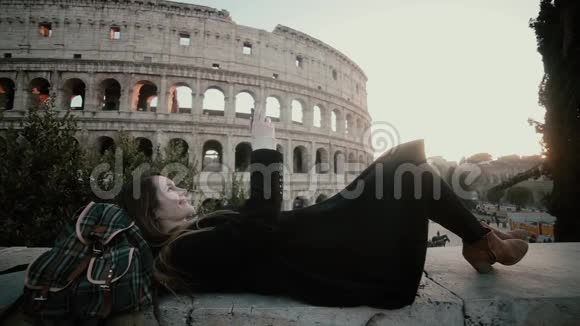 意大利罗马斗兽场附近躺着一位年轻的旅游妇女女孩在智能手机上的视线附近拍一张自拍照片视频的预览图