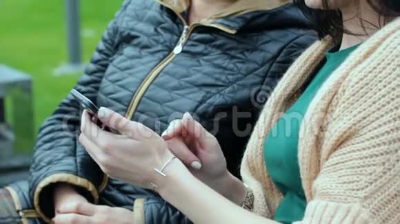 一个小女儿正在教她妈妈如何使用智能手机两个不同年龄的黑发女郎坐在长凳上视频的预览图