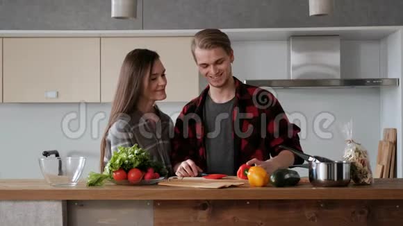 年轻漂亮的一对穿格子衬衫的夫妇正在家厨房做饭一个女人和一个男人切菜做菜视频的预览图