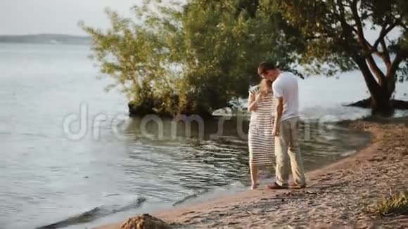 男人和女人晚上在河岸上散步美丽的一对情侣在日落时拥抱在水边视频的预览图