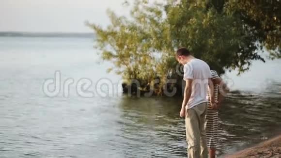 年轻漂亮的一对夫妇站在河岸上摸着水浪漫的男女约会视频的预览图