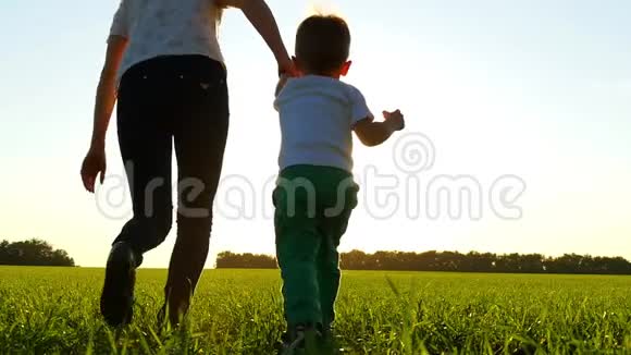 日落时分母亲和孩子沿着绿草地慢悠悠地跑过田野视频的预览图