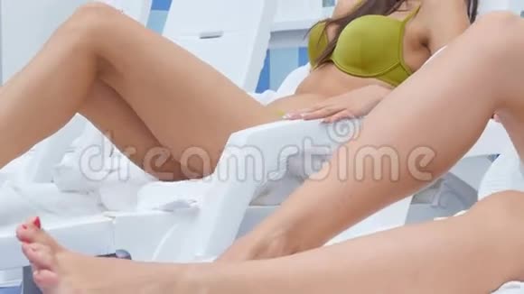 两个漂亮的女孩坐在游泳池附近的躺椅上聊天和微笑视频的预览图
