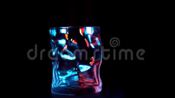 玻璃杯在黑色背景下的蓝色和红色背光下旋转视频的预览图