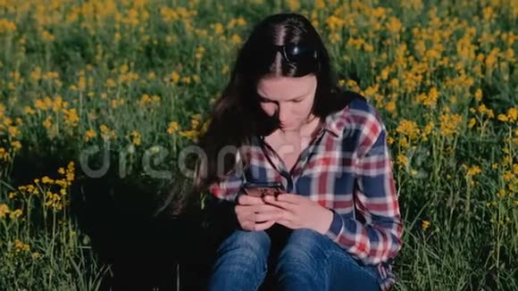 女人看着手机坐在公园里的草地上黄花视频的预览图