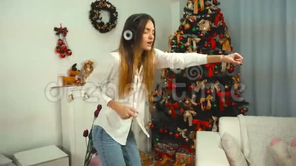 有趣的女孩用耳机听音乐在圣诞树上跳舞视频的预览图
