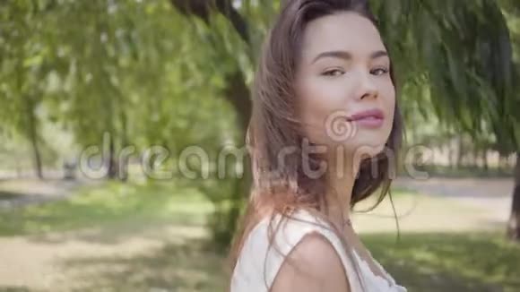 肖像迷人的年轻女孩一头长长的黑发穿着一件白色的夏季时装长裙站在下面视频的预览图