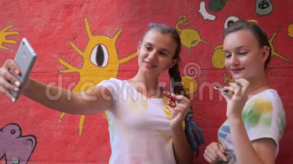 在涂鸦背景下抱着旋转体的女孩塞尔菲女朋友用玩具在手机上拍照以缓解压力视频的预览图