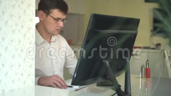 一个穿白衬衫的男人在他的办公室里的电脑后面工作视频的预览图