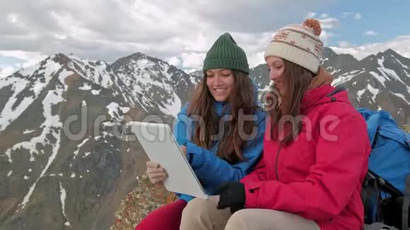 在挪威的高山和湖泊背景下一个坐在岩石上的平板电脑上的女徒步旅行者视频的预览图