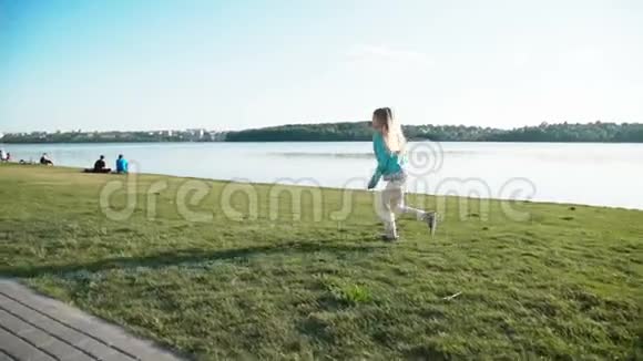 一个金发碧眼的小女孩在池塘的明亮天空下的码头上奔跑视频的预览图