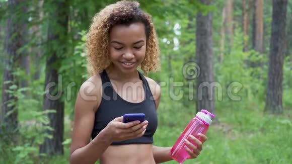 年轻的黑人妇女在慢跑后使用智能手机并将绿色屏幕显示到相机上视频的预览图