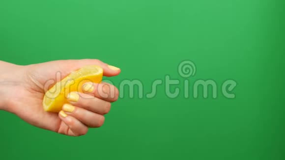 带有黄色指甲的女性手在绿色关键背景上挤出半个柠檬视频的预览图