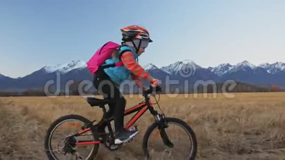 一个高加索儿童在麦田里骑自行车小女孩骑着黑色橙色自行车在美丽的雪背景下视频的预览图