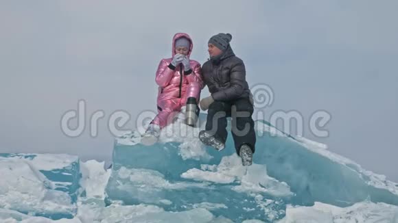 在冰封的湖面上年轻夫妇在冬天散步时玩得很开心情侣们坐在蓝色的大冰块上视频的预览图