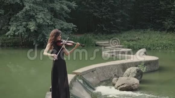 优雅美丽的女孩穿着黑色连衣裙拉小提琴呆在桥上户外视频的预览图