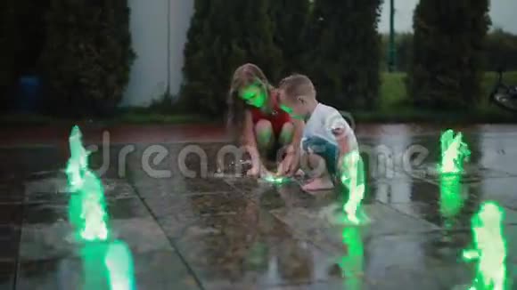 哥哥和姐姐一起在彩色喷泉玩男孩和女孩在炎热的夏天接触喷水弄湿了孩子们视频的预览图