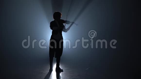 女孩拉小提琴在黑暗中看着音乐台剪影黑烟背景视频的预览图