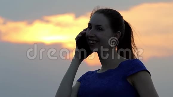 日落时分一位年轻女子微笑着用智能手机给某人打电话视频的预览图
