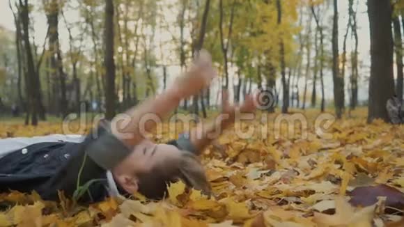 快乐的男孩躺在秋天公园的黄叶上视频的预览图