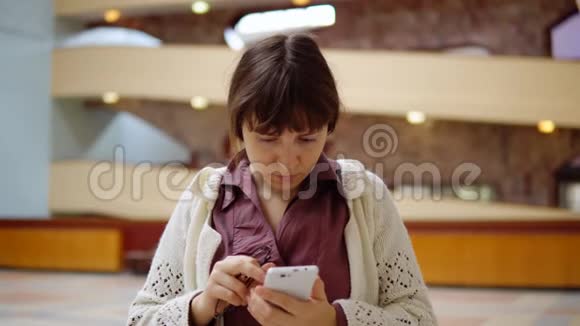 布吕内特女商人穿着深色上衣在室内使用智能手机视频的预览图