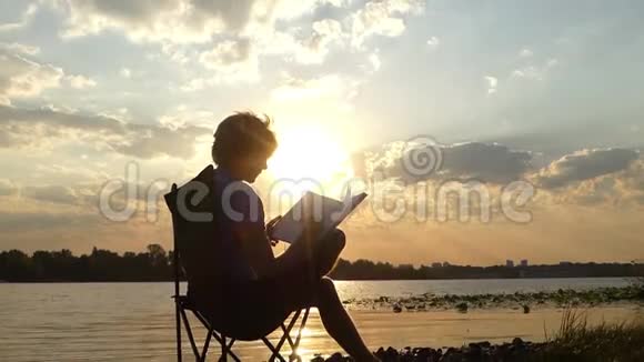 男人坐着想着在他的记事本上写着什么在一个沼泽的河岸上视频的预览图